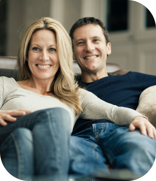 A Couple smiling and sitting on the couch in their house.
